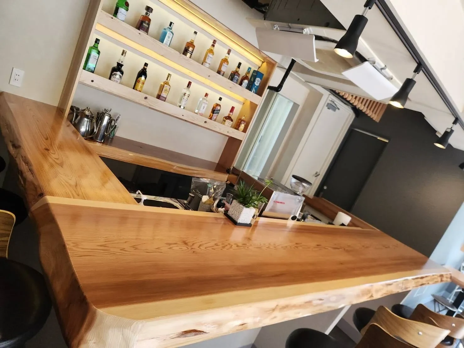 一枚板のカウンターと、奥のボトル棚。スツールが並ぶ店内